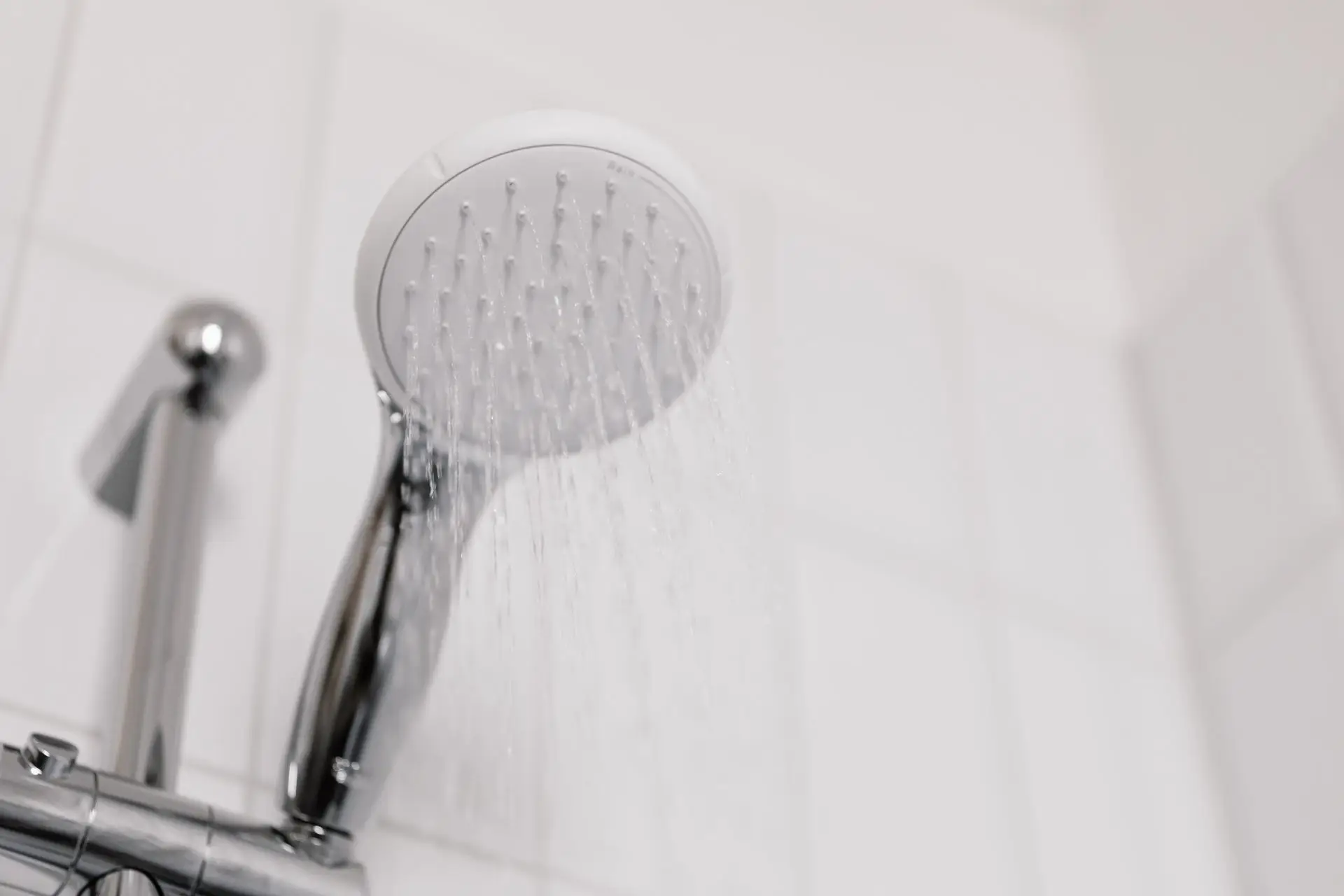 Shower head running water in a white tiled bathroom